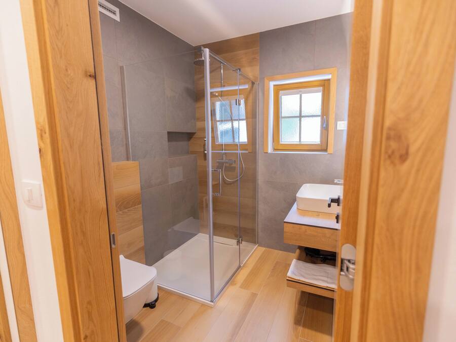 Een moderne badkamer met een glazen douchecabine, een houten wastafelmeubel en een klein raam.
