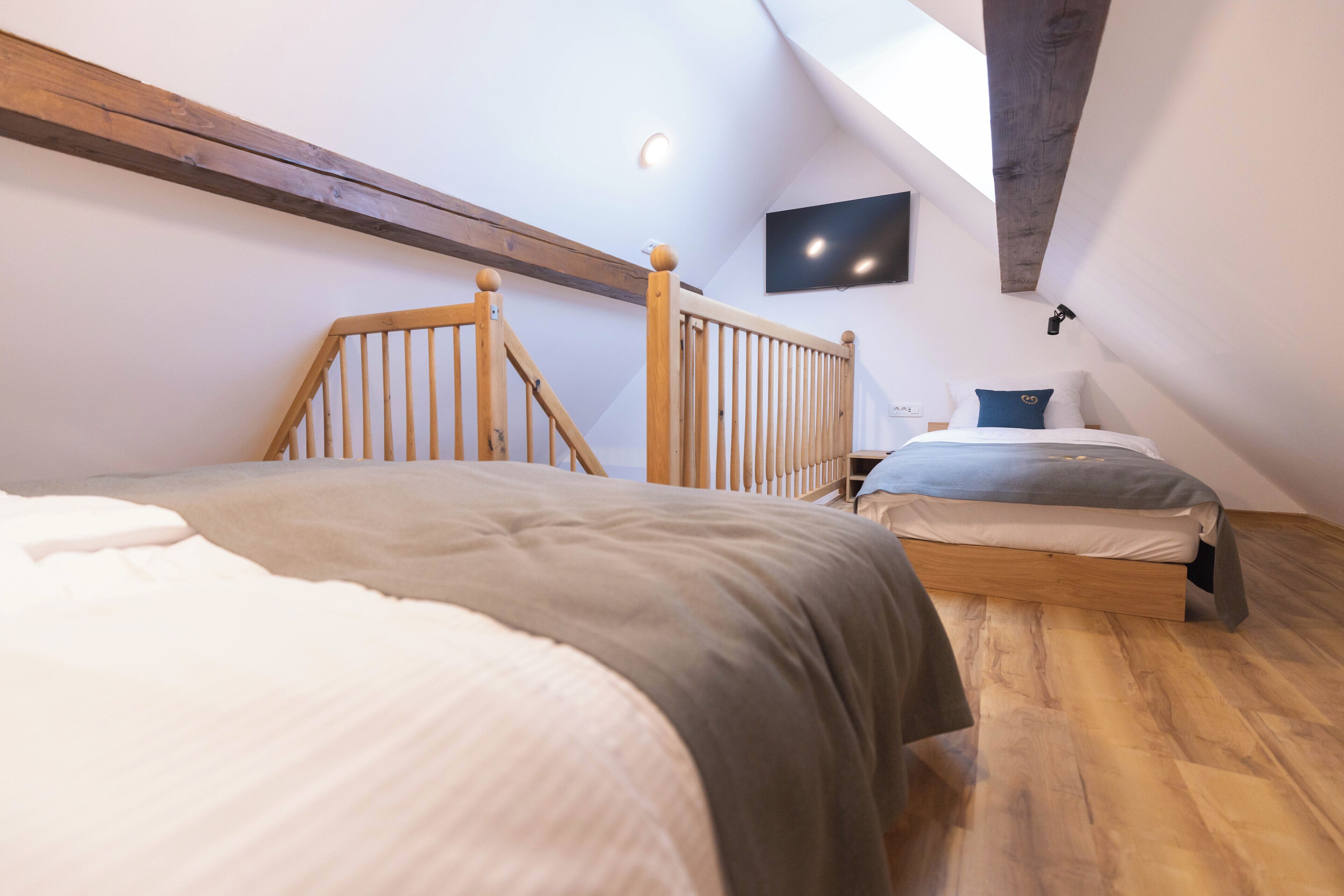 A bedroom with two beds, wooden beams, a flat-screen TV, and a skylight.