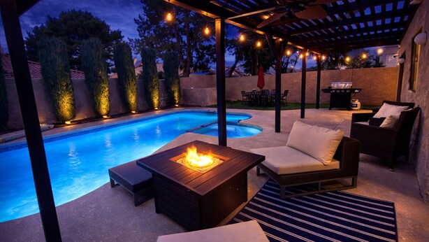 An outdoor pool area with a fire pit table, lounge chairs, and a pergola with string lights. - Heated Pool & Spa, Billiards, 15 Min Vegas Strip (Henderson)