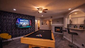 A pool table with a television displaying 'World Series of Poker' in a room with a fireplace and bar seating.