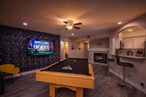 Een pooltafel met een televisietoestel waarop 'World Series of Poker' wordt vertoond, in een kamer met een open haard en een bar.