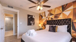 A hotel room with a large bed, a ceiling fan, a wall-mounted artwork, and a bathroom visible through an open door. - Heated Pool & Spa, Billiards, 15 Min Vegas Strip (Henderson)