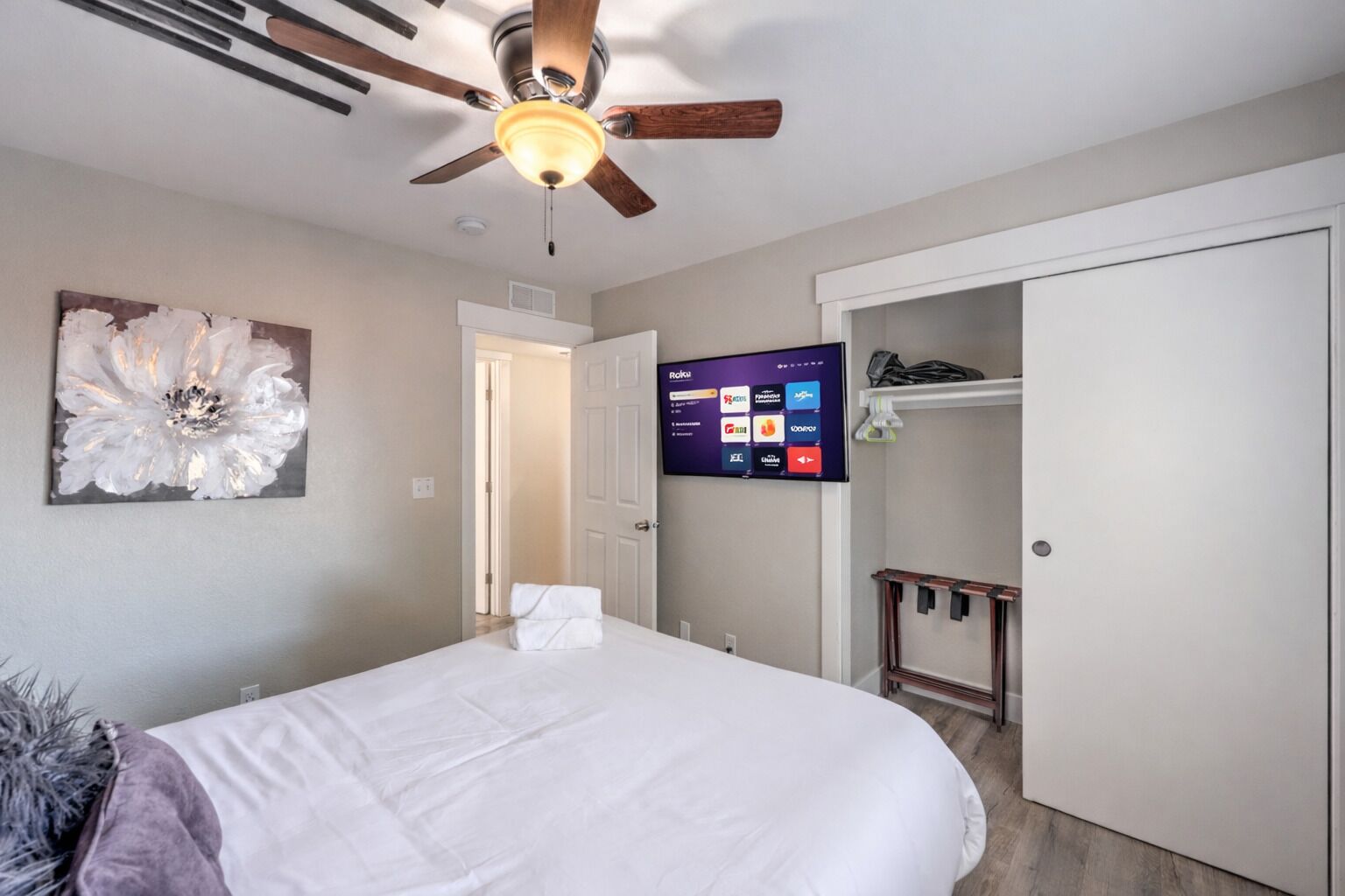 A hotel room with a bed, a ceiling fan, a wall-mounted TV, and a door leading to a closet.