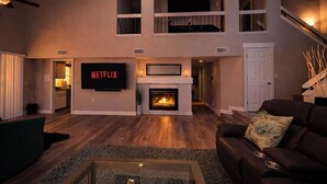 A spacious living room with a fireplace, a flat-screen TV, and a staircase leading to an upper level. - Heated Pool & Spa, Billiards, 15 Min Vegas Strip (Henderson)