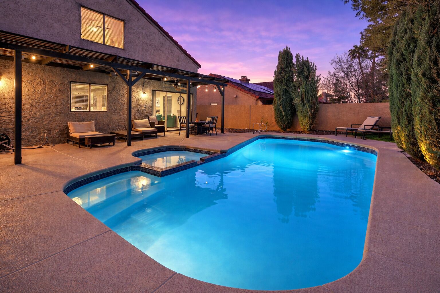 A swimming pool with a curved edge, surrounded by a covered patio area with seating.