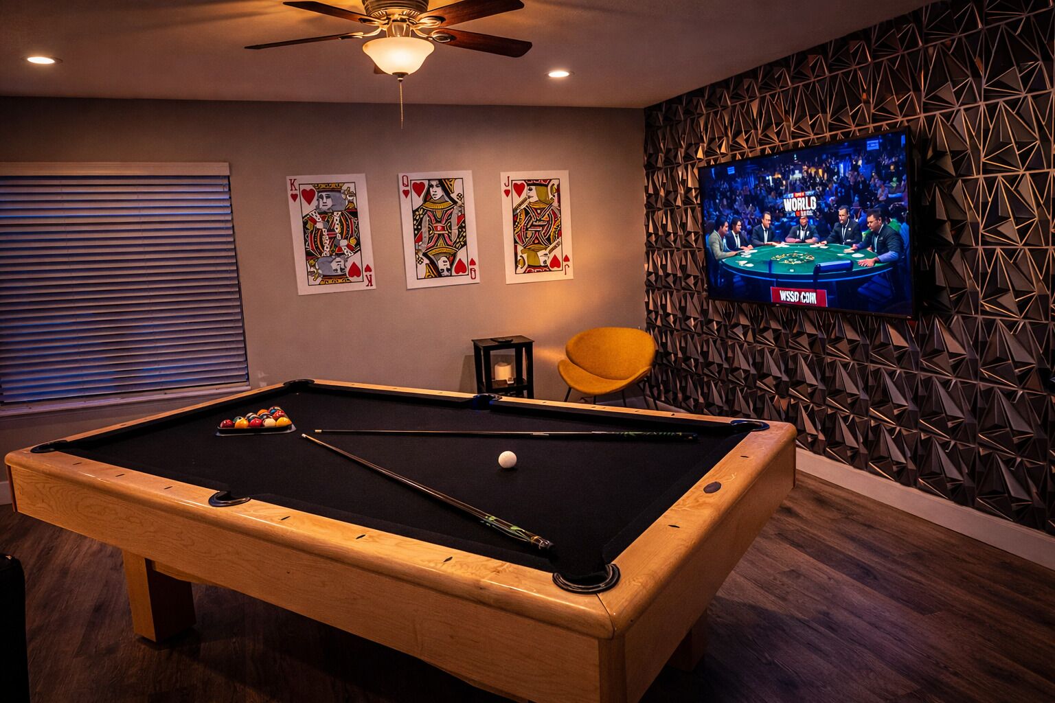 A pool table with balls, a television displaying a poker game, and three playing cards on the wall.