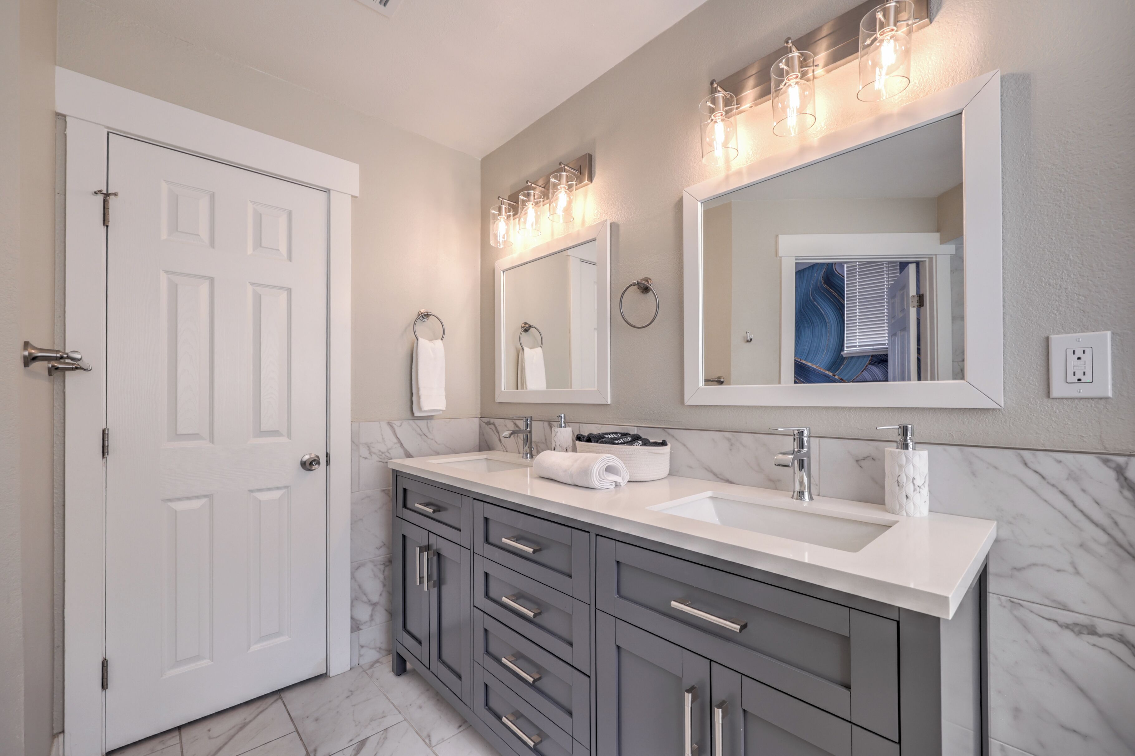 Un baño moderno con una puerta blanca, un tocador con lavabo, un espejo y un perchero para toallas.