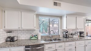 A modern kitchen with white cabinetry, a granite countertop, a stainless steel sink, and a window with blinds. - Heated Pool & Spa, Billiards, 15 Min Vegas Strip (Henderson)