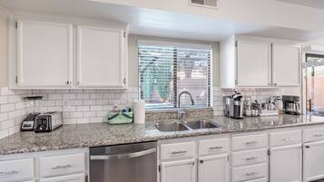 A modern kitchen with white cabinetry, a granite countertop, a stainless steel sink, and a window with blinds.