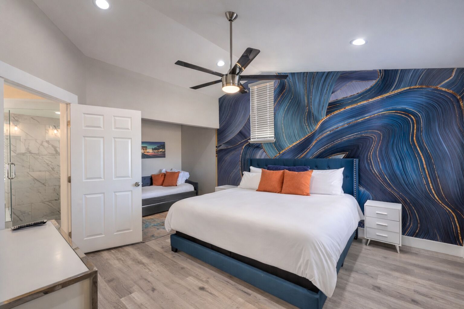 Une chambre à coucher comprenant un lit, une table de chevet, un ventilateur de plafond et un mur orné d’un motif imitant le marbre.