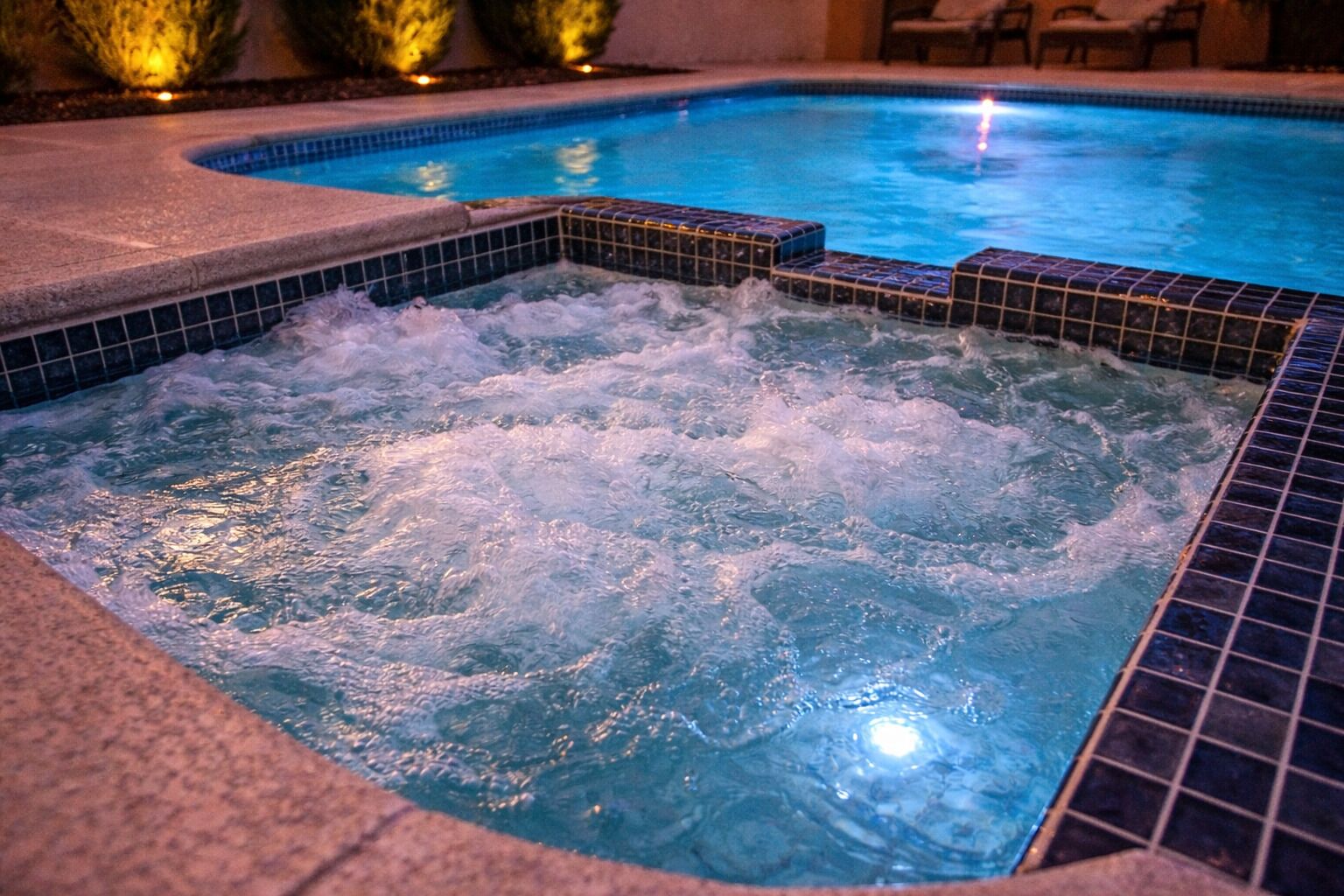 A hot tub with bubbling water, surrounded by a tiled pool area.