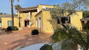 A yellow building with a spiral staircase, a palm tree, and a stone pathway. - Vi Ja Villa Janas  (Sestu)