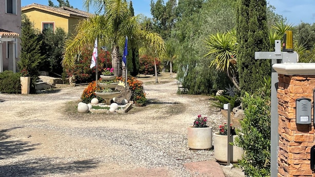 A courtyard with a fountain, potted plants, and a stone wall. - Vi Ja Villa Janas  (Sestu)