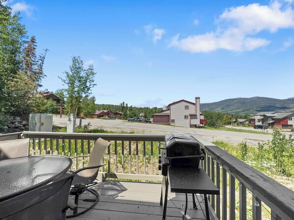 A deck with a grill and a chair, overlooking a road with houses and mountains in the background. - Beautiful Mountain Townhome, Great Views, Lots of Space 173 (Silverthorne)
