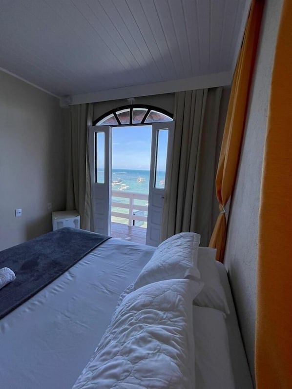 Habitación de hotel con cama, ventana con cortinas y vista a la playa.