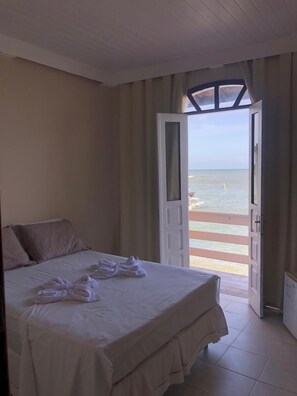 Una habitación de hotel con una cama, vista a la playa y una puerta que da al exterior.
