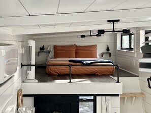 A compact, modern bedroom with a bed, bedside tables, a heater, and a window.