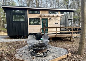 A modern cabin with a deck, outdoor seating, and a fire pit.