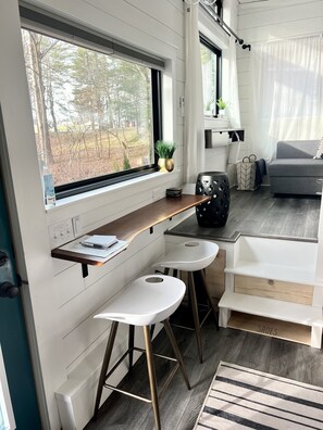 Una cocina moderna con ventana, encimera de madera, dos taburetes blancos de bar y un sofá gris.