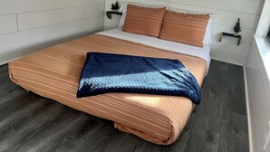 Una cama con una colcha a rayas, un plaid azul oscuro y almohadas a juego.