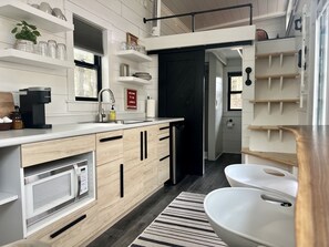 A modern kitchen with a built-in microwave, a coffee maker, and a sink. There is a black door leading to another room.