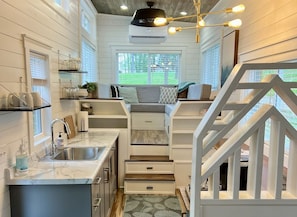 Una cocina compacta con lavamanos, encimera y almacenamiento integrado. Una escalera conduce a una zona de estar con vistas al exterior.