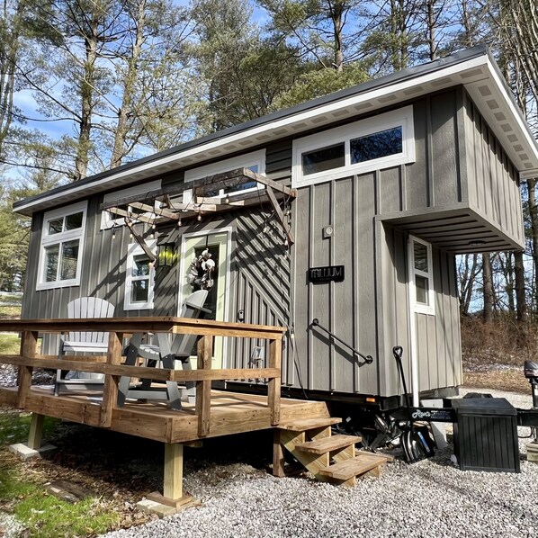 A small cabin with a porch, a wooden deck, and a gravel driveway.