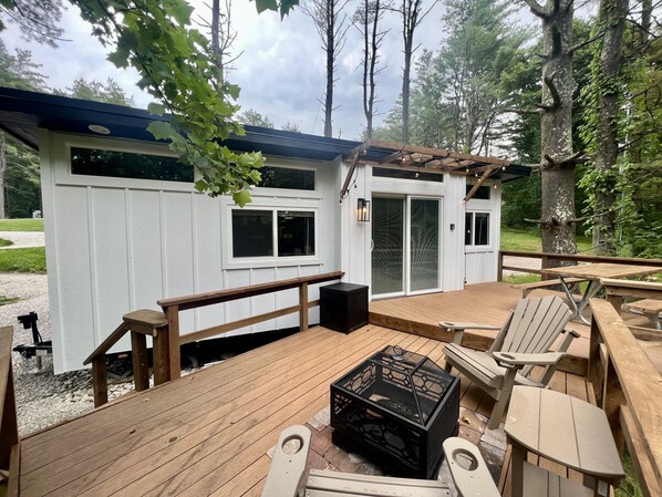 Una terraza de madera con zona de estar cubierta, una parrilla y un pequeño cobertizo con puertas correderas de vidrio.