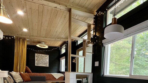 A compact living space with a kitchenette, a sofa, a dining table, and a window providing a view of greenery. - Dahlia Tiny House by the Lake (Logan)