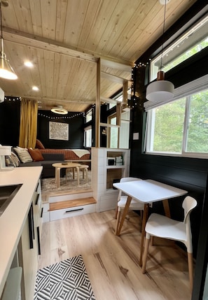 Eine kompakte, moderne Küche mit Holzboden, einem Essbereich mit weißem Tisch und Stühlen und einer gemütlichen Sitzecke mit Sofa und Kissen.