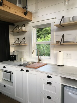 A modern kitchen with white cabinetry, a wooden countertop, a sink, and a window with a view of greenery.