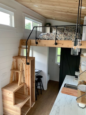 A compact kitchen with a wooden bench, a small dining table, and a built-in bench with shelves. - The Gladiola Tiny House by the Lake (Logan)