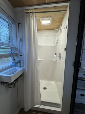 A modern bathroom with a shower, a window with blinds, a sink, and a toilet. - The Gladiola Tiny House by the Lake (Logan)