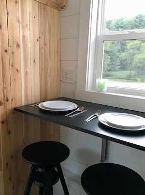 A kitchen with a black countertop, two white plates, cutlery, and a window with a view of greenery. - The Gladiola Tiny House by the Lake (Logan)