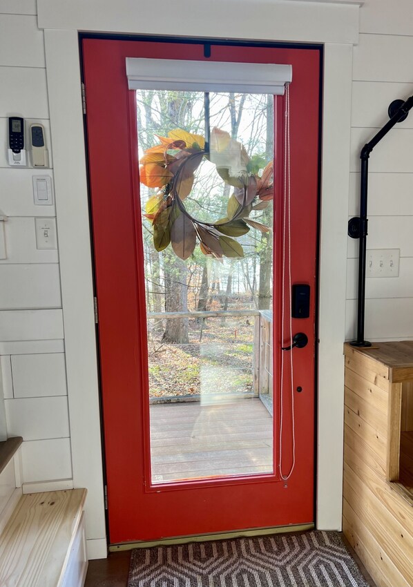 Una puerta roja con un panel de vidrio, un banco de madera y un tapete estampado.