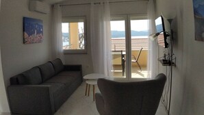 A living room with a grey sofa, a small round table, and a chair. There is a painting on the wall and a TV mounted on the wall. - Apartment in Okrug Gornji with Seaview, Balcony, Air condition, WIFI (5059-4) (Okrug Gornji)