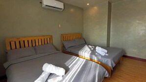 Une chambre d’hôtel avec deux lits simples, une literie grise, des têtes de lit en bois et un climatiseur fixé au mur.