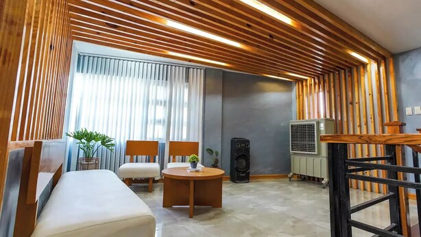 Une chambre d’hôtel moderne avec un plafond en bois, un canapé, deux fauteuils, une petite table avec une plante, un haut-parleur et un appareil de climatisation.