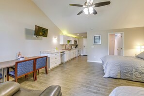 A modern, well-lit room with a dining area, kitchenette, and a large bed.