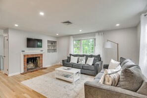 A living room with a fireplace, grey sofas, a white coffee table, and a large window with curtains. - Middletown Vacation Rental: 2 Mi to Beach! (Middletown)