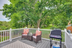 A deck with wicker chairs and a grill, surrounded by lush greenery.