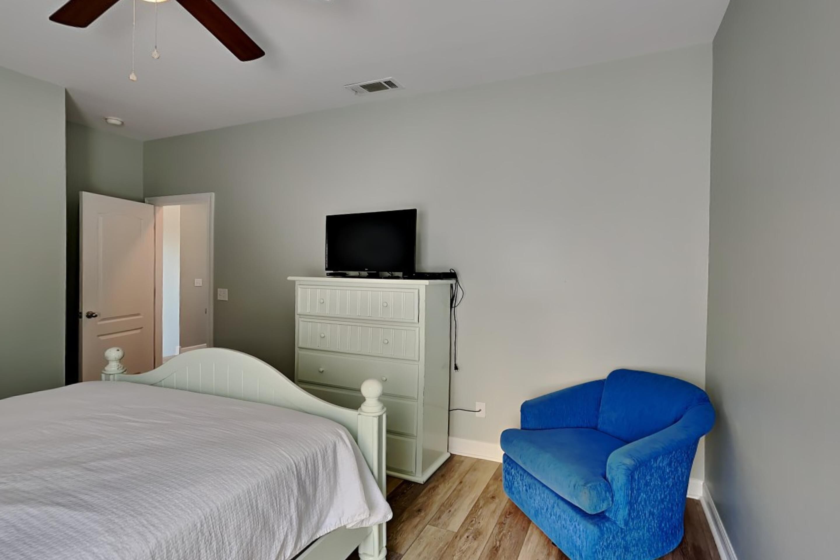 A bedroom with a bed, a dresser, a television, and a blue chair.