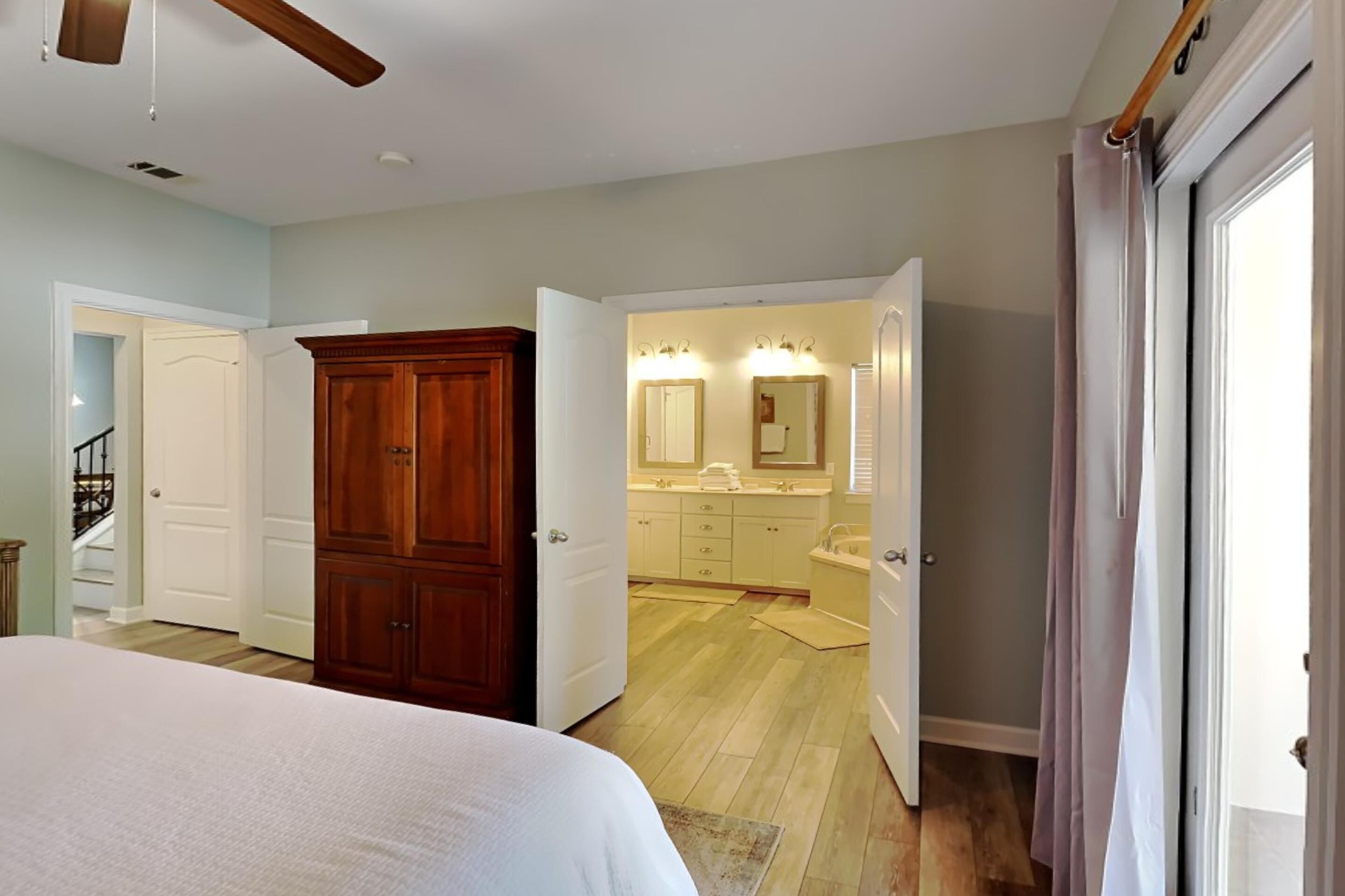 A bedroom with a large bed, a wooden wardrobe, and an open door leading to a bathroom with a sink and mirror.