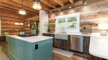Una cocina con vigas de madera, una isla grande, electrodomésticos de acero inoxidable y una ventana con persianas.