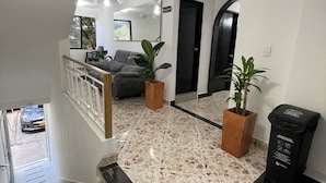 Een modern interieur met een trap, een zithoek met een bank en planten, en een betegelde vloer.