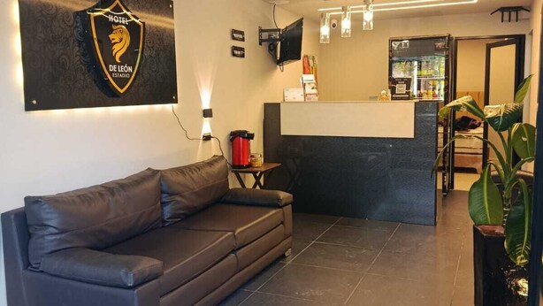 Een moderne hotellobby met een receptiebalie, een leren bank, een potplant en een logo dat aan de muur is bevestigd.