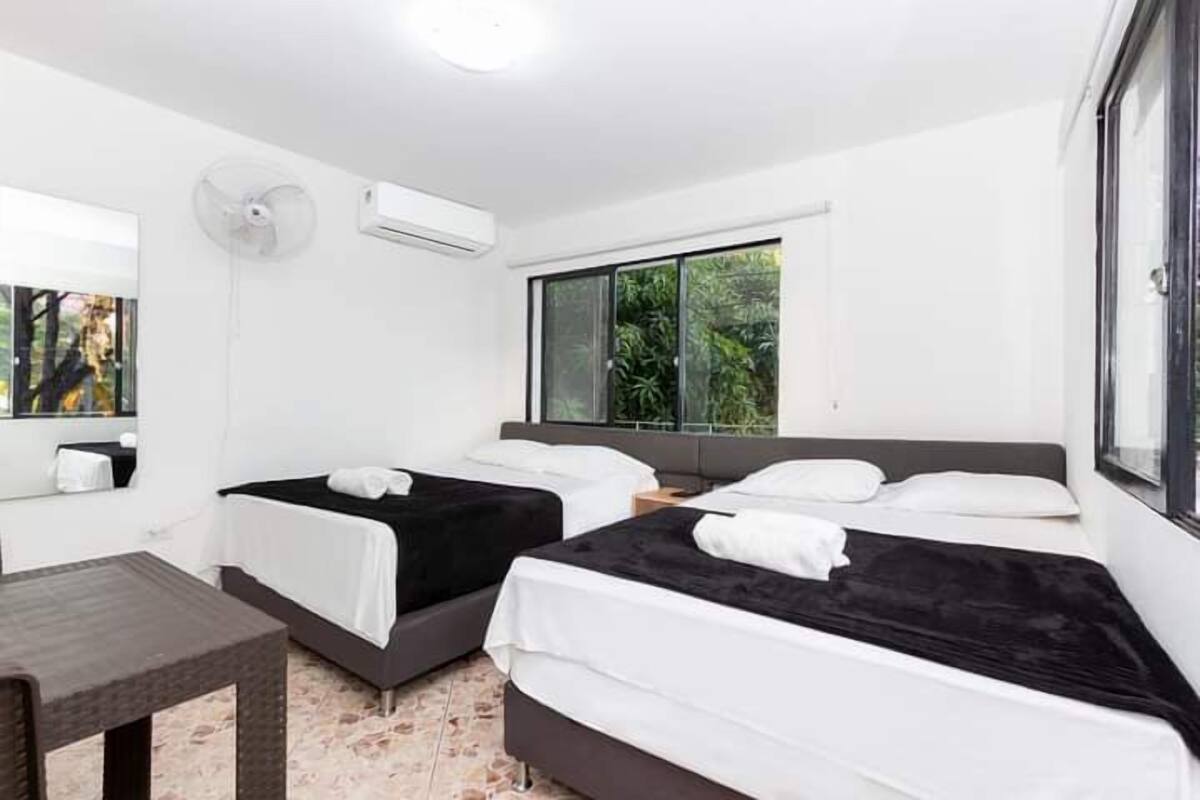Une chambre d’hôtel avec deux lits, une petite table, un ventilateur et un appareil de climatisation.