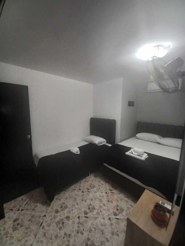 A small, dimly lit room with two single beds, a small table, and a heater. - Hotel De León Estadio (Medellín)