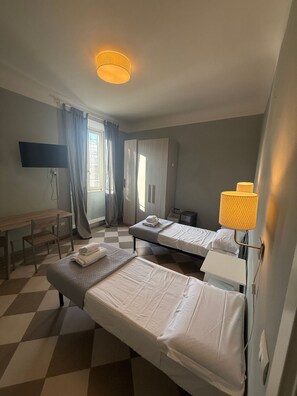 Hotellihuone, jossa on kaksi sänkyä, työpöytä, tuoli, televisio ja lamppu.