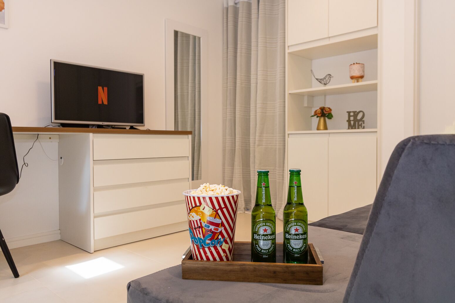 A living room with a TV displaying the Netflix logo, a popcorn container, and two Heineken beer bottles on a wooden tray.